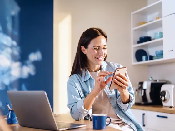 A person at home in a kitchen, smiling, with a laptop open on the counter